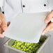 A person holding a white Flexsil lid over a container of green beans.