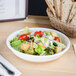 A white Tuxton pasta/salad bowl filled with salad on a table.