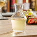 An Arcoroc glass wine carafe filled with white wine on a table.