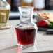 An Arcoroc glass wine carafe filled with red wine on a table.
