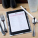 An Alumitique aluminum menu board on a table with a spoon and glass of water.