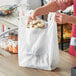 A person holding a white plastic Choice T-shirt bag full of cupcakes.