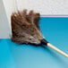 A Carlisle feather duster with a wood handle on the floor.