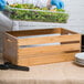 A person in a blue uniform holding a container of salad in a American Metalcraft bamboo wood crate on a table.