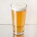 A Libbey mixing glass of beer with foam on a table.