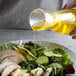 A person pouring 100% pure avocado oil onto a salad with avocado and chicken.