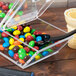 A clear plastic Cal-Mil cereal dispenser filled with candy on a glass shelf.