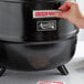 A hand putting a sticker on a black soup kettle.