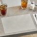 A gray Choice paper placemat with a scalloped edge on a table with a glass of brown liquid and ice.