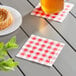 Choice Red Gingham beverage napkin on a table with a glass of coffee and a plate of pastries.