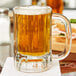 A Libbey paneled beer mug full of beer on a table.