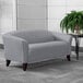 A Flash Furniture gray leather loveseat with wooden legs in a lounge area with a potted plant.