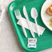 A white plastic fork, spoon, and knife wrapped in a white napkin with salt and pepper on a green and white tray.