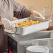 A woman in a chef's uniform holding a Vollrath stainless steel steam table pan on a counter.