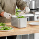 A person in a chef's uniform using a Vollrath stainless steel pan to serve spinach leaves.