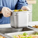 A person in a blue uniform holding a Vollrath stainless steel container of food.