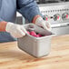 A person wearing gloves holding a Vollrath stainless steel hotel pan filled with food.