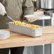 A person in a chef's uniform holding a Vollrath stainless steel steam table pan full of food.