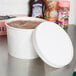 A close up of a white Choice paper food container with a lid on a counter.