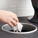 A hand dropping a white tissue in a Vollrath round stainless steel in-counter trash chute.