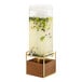 A Cal-Mil square beverage dispenser with a wooden stand filled with a drink on a counter.