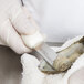 A person in white gloves using a Dexter Russell clam knife to cut an oyster shell.