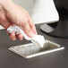 A hand holding a tissue over a Vollrath rectangular stainless steel in-counter trash chute.