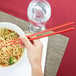 a person holding chopsticks in a bowl of noodles