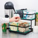 A person putting a packet into a black Cal-Mil condiment holder with glass jars.