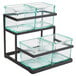 A black metal 2-step stand with 3 glass containers holding condiments.