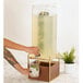 A person pouring a drink from a Cal-Mil Mid-Century beverage dispenser with walnut and brass base and infusion chamber.