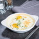A white Tuxton round china dish with shirred eggs and herbs on top.