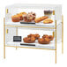 A two-tiered clear pastry case with a brass frame, displaying assorted baked goods.