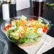 A salad in a Dart plastic bowl with a fork on a table.