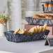 A black rectangular basket filled with bread on a table.