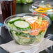 A salad in a Dart plastic bowl with a SafeSeal lid on a table.