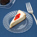 A slice of cheesecake on a clear Fineline Flairware plastic plate with a fork.