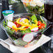 A Dart plastic bowl of salad with a plastic fork and knife on a counter.