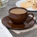 A brown Tuxton mahogany cappuccino saucer on a table with a cup of coffee and cookies.