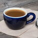 A blue Tuxton cappuccino cup with a drink in it on a counter.