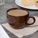 A brown Tuxton mahogany cappuccino cup on a napkin next to cookies.
