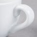 A close-up of a Tuxton white porcelain cappuccino cup with a handle.