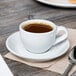 A Tuxton porcelain white cappuccino cup on a saucer with a spoon.