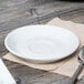 A white Tuxton porcelain saucer with a spoon on a table.