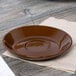 A brown Tuxton Mahogany Cappuccino saucer on a table.