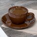 A brown cup of coffee on a Tuxton mahogany cappuccino saucer.