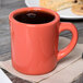 A Tuxton Cinnebar china mug filled with coffee on a napkin next to a plate of cookies.