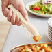 A hand using Cambro beige scallop grip tongs to serve croutons from a plate on a table.