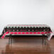 A rectangular table with a black and red plastic Creative Converting Ohio State University table cover with red and white logos on it.