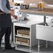 A man using an Advance Tabco stainless steel drainboard shelf next to a sink in a professional kitchen.